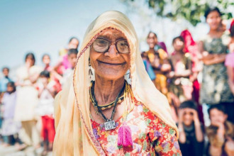 आफ्नो ठूलो परिवारअगाडि बसेर क्यामरामा हाँस्दै एक भारतीय पाको उमेरकी महिला